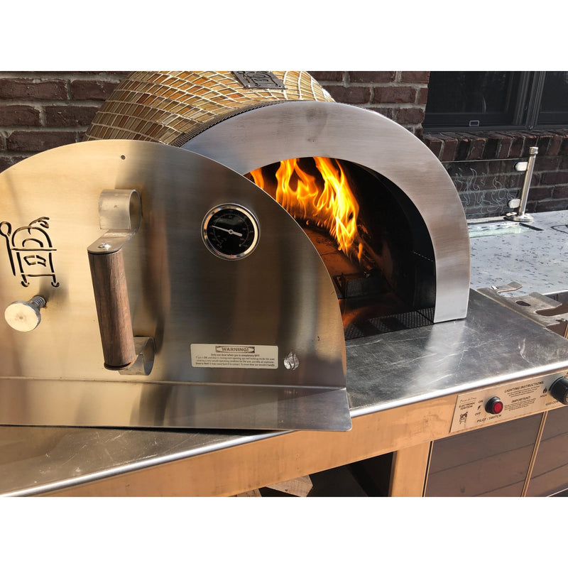 Stainless steel outdoor pizza oven with fire inside, brick wall background